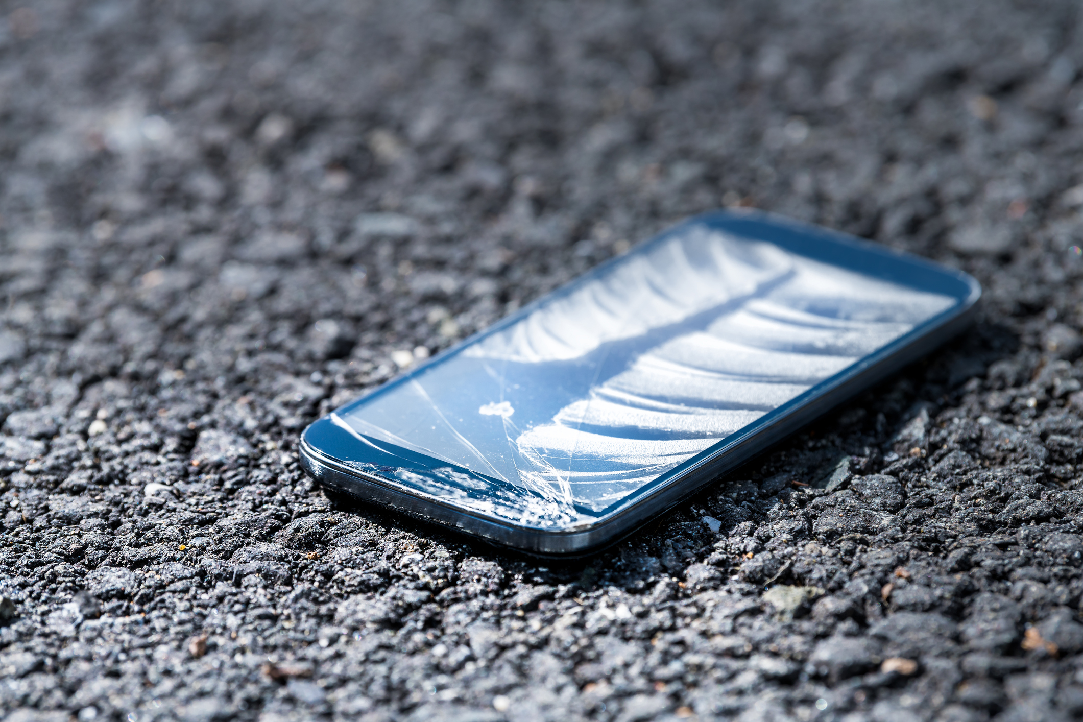 Mobile phone with smashed screen laying on tarmac